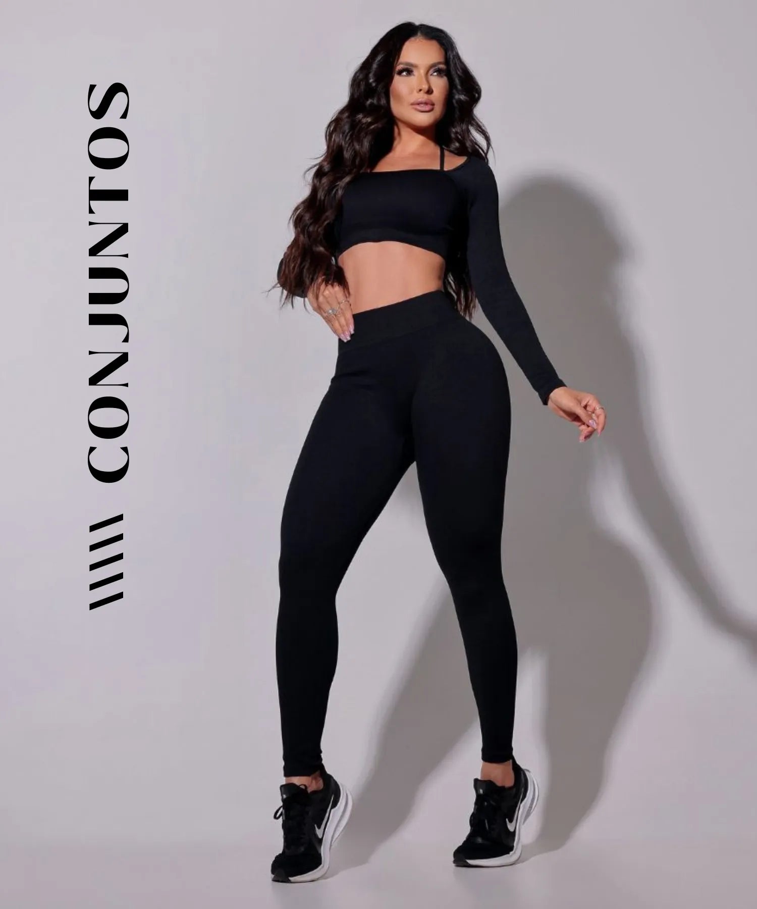 Modelo vestindo conjunto fitness preto, composto por top e legging, em pose relaxada.